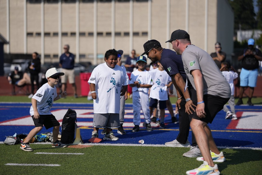 Keenan, right in a grey shirt, coaching young players at a youth baseball camp