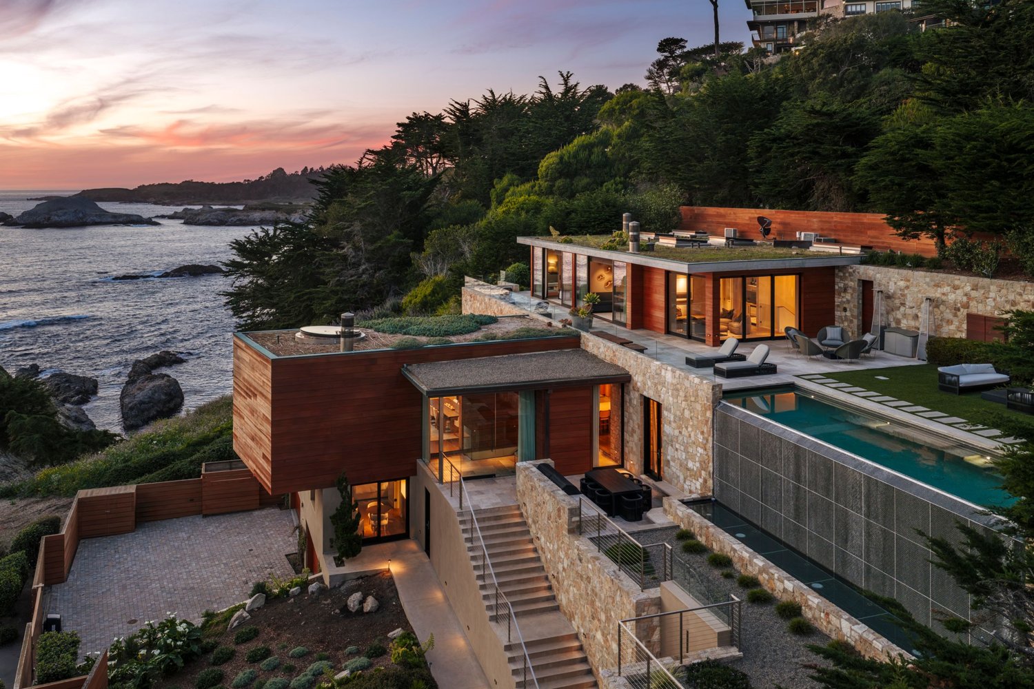 Oceanfront Pacaso home at sunset with terraced stone, green roofs, and an infinity pool