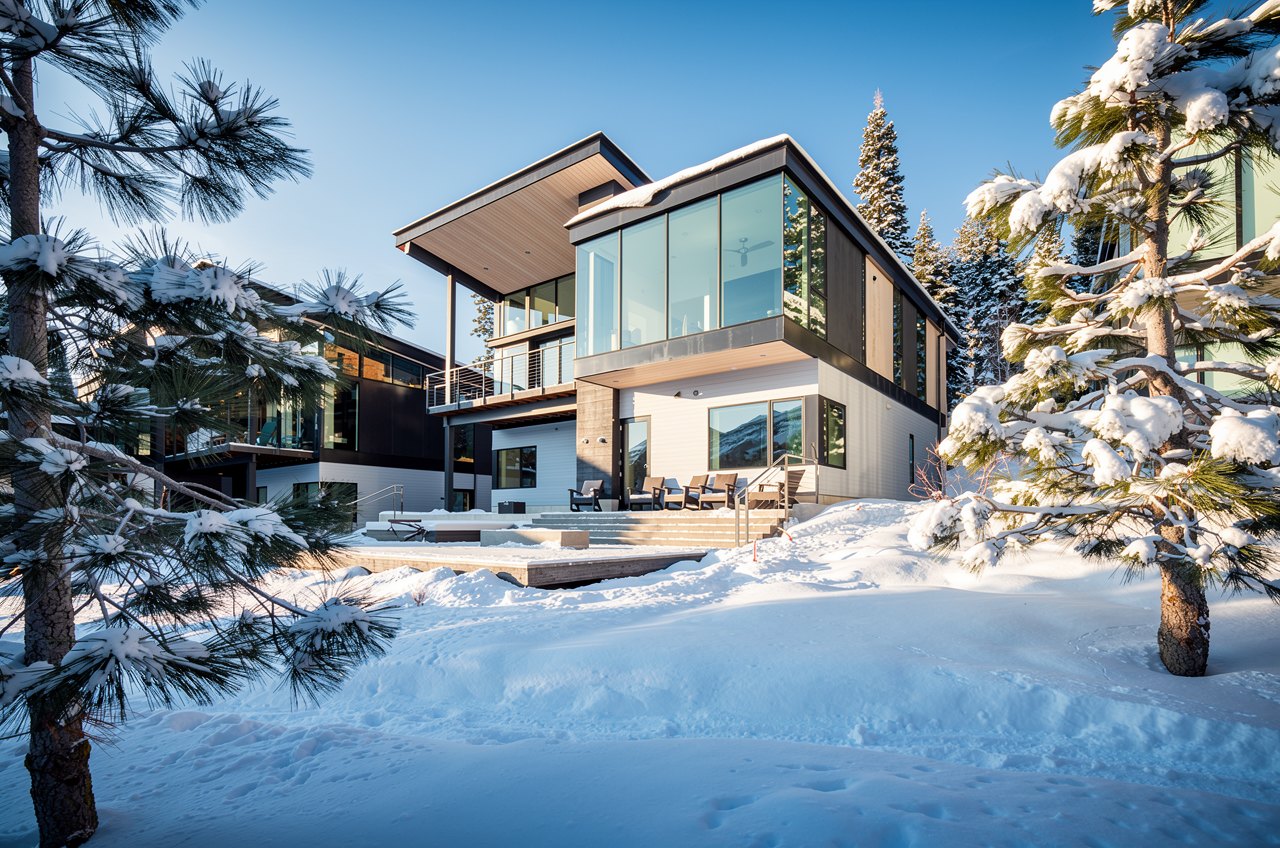 Modern Pacaso home with walls of glass in fresh snow among pines