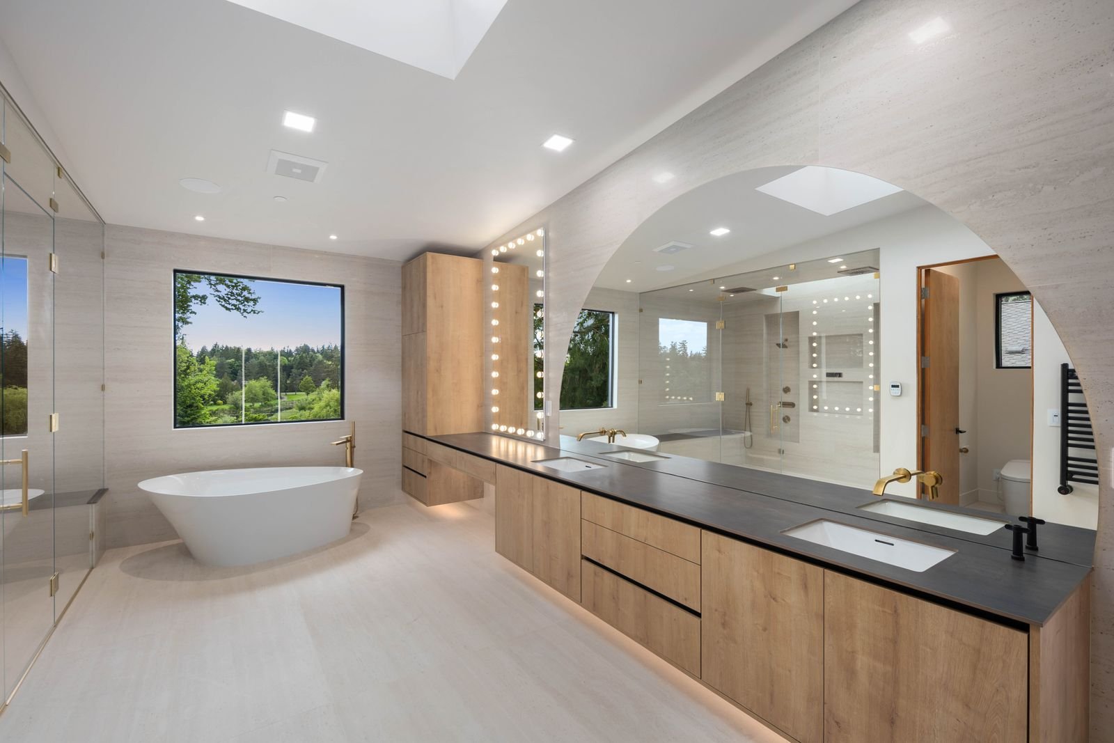 Primary bath in a custom home with a freestanding tub, oak vanity, and arched mirror
