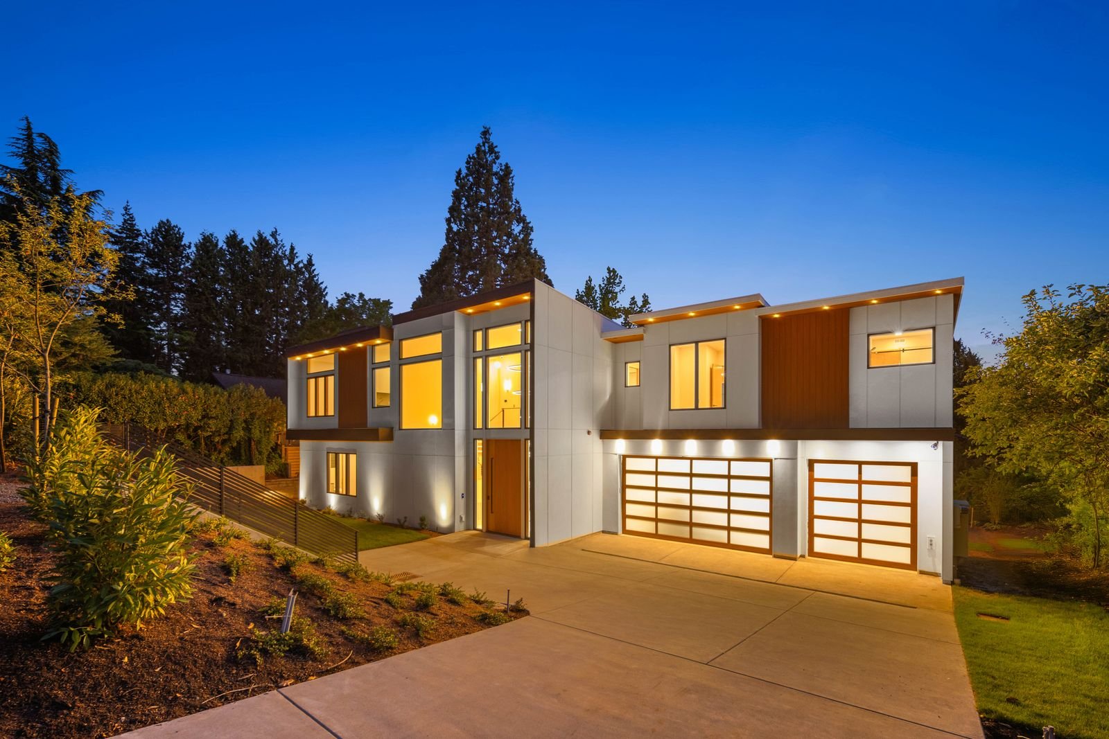 Modern two-story custom home by The Custom Home Company at dusk with warm interior light